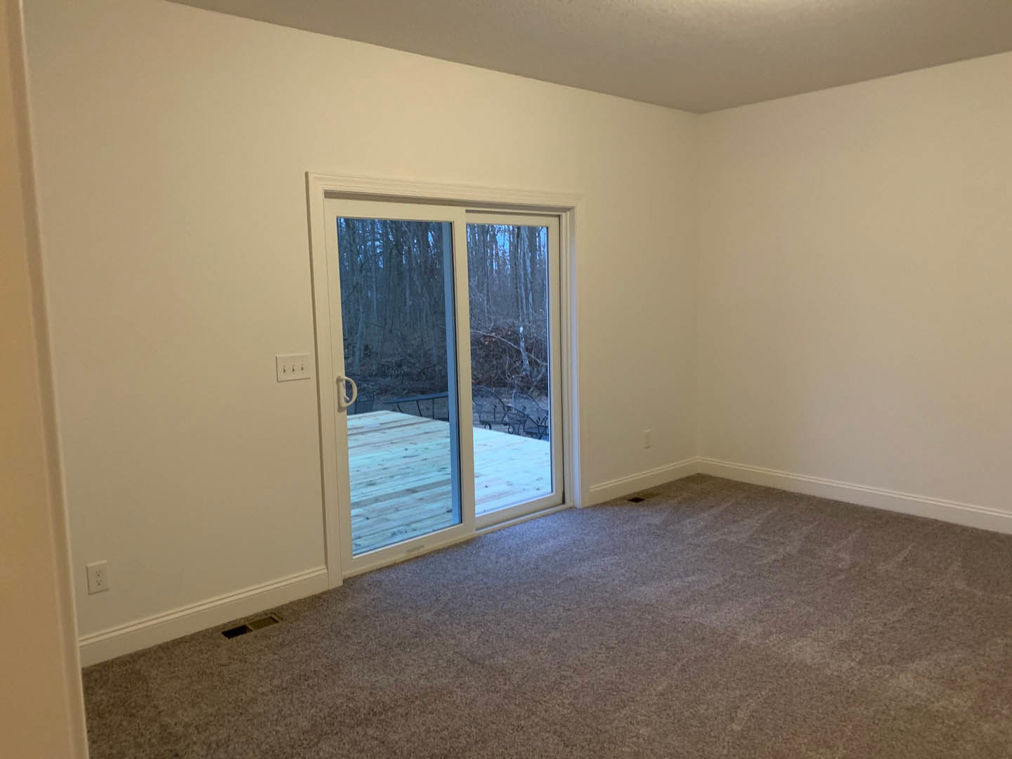 Living room with light laminate flooring, white plaster walls, and large sliding glass door opening to a deck with trees visible outside