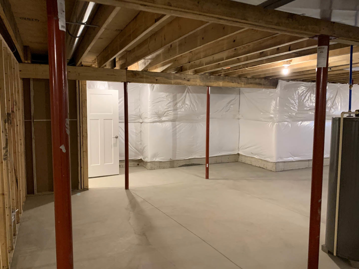 White wall with exposed wooden ceiling beams, white door featuring a silver handle, concrete floor with a thin dividing line, white sheet partially covering the wall in an empty