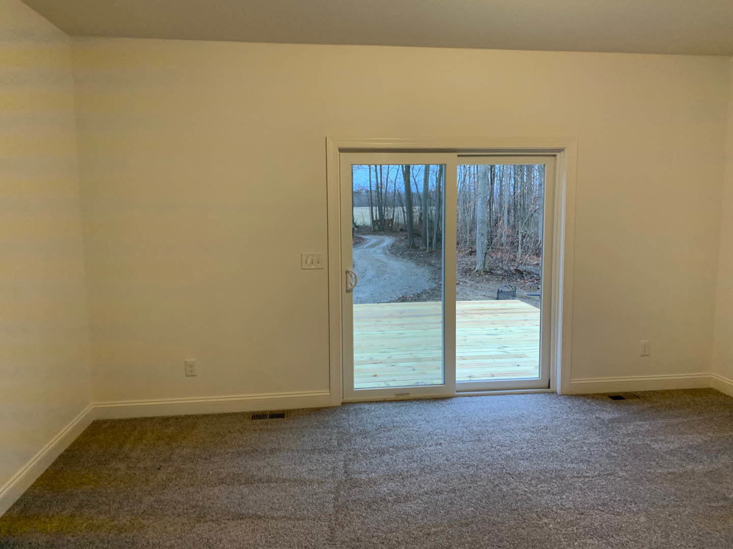 Carpeted room with white walls, large sliding glass door opening to wooded view and visible outdoor path