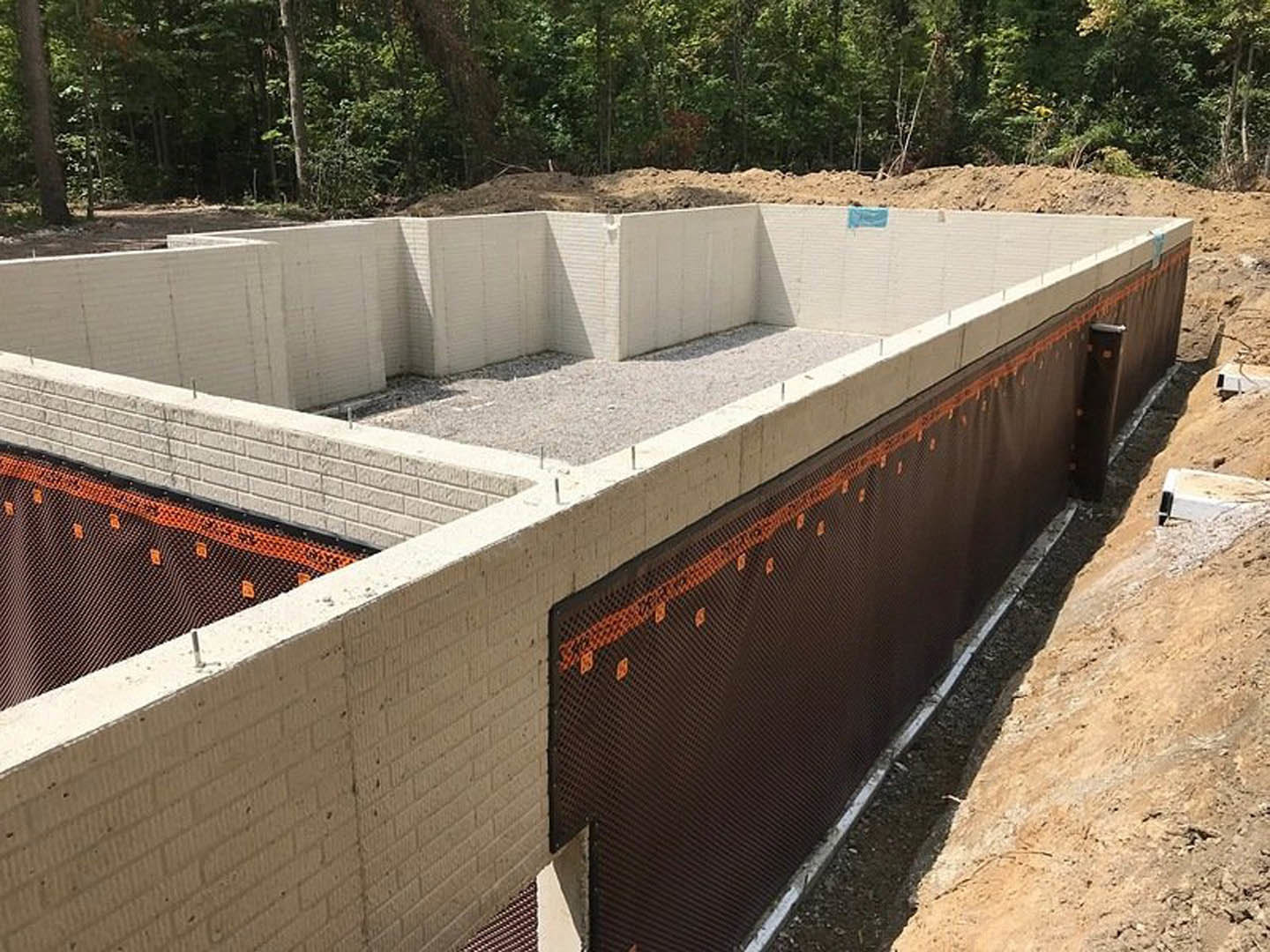 Concrete foundation slab surrounded by dirt and construction materials, bordered by trees and unfinished walls