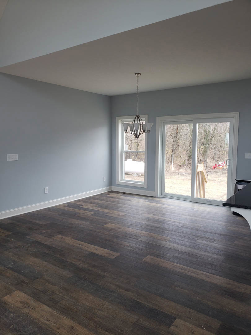 Wood floor room with chandelier, sliding glass door opening to outdoor view, white walls, ceiling light fixture, large window.