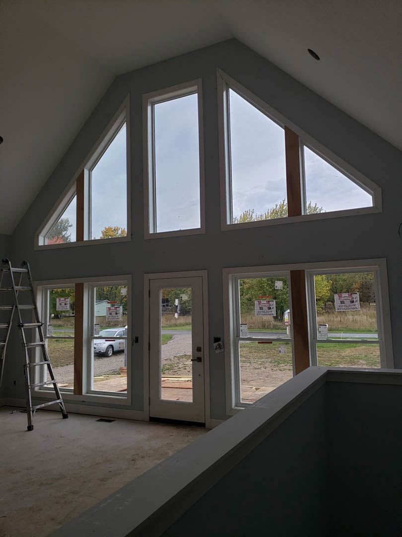 Wooden ladder leaning against a large window in a bright room with white walls and natural daylight streaming in