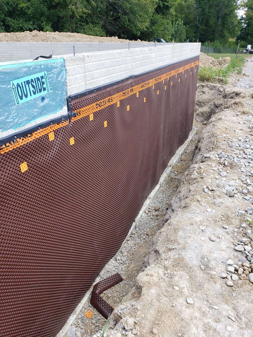 Brown exterior wall with blue sign featuring black text, surrounded by leafless trees and outdoor ground.