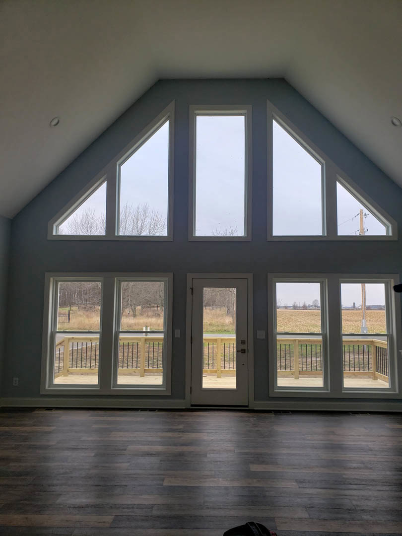 Spacious room with wood flooring, large windows, white walls, and a door opening to a field view; black bag placed on the floor.