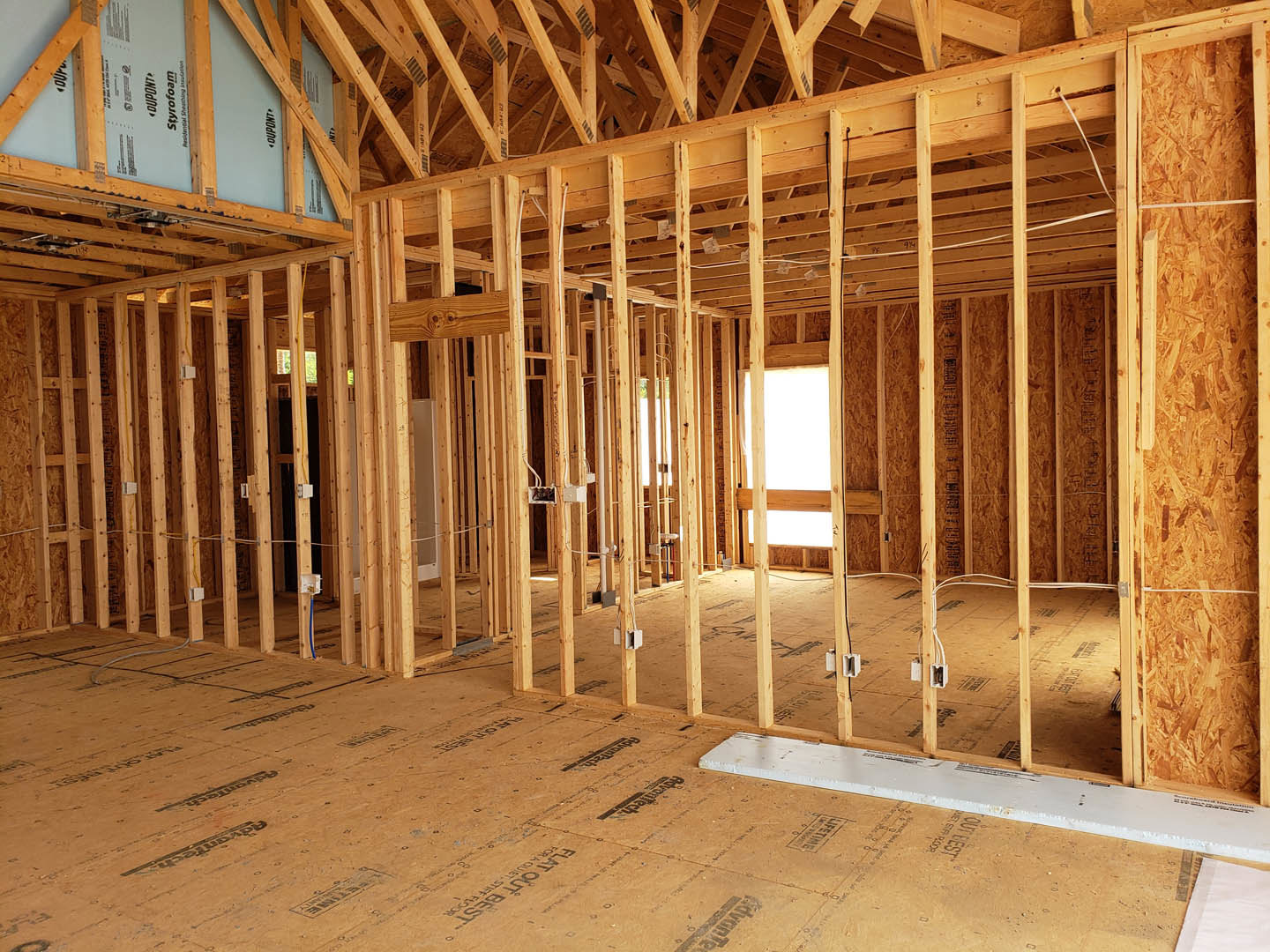 Exposed wood framing and beams inside a house under construction, unfinished ceiling and floor, white board resting on subfloor
