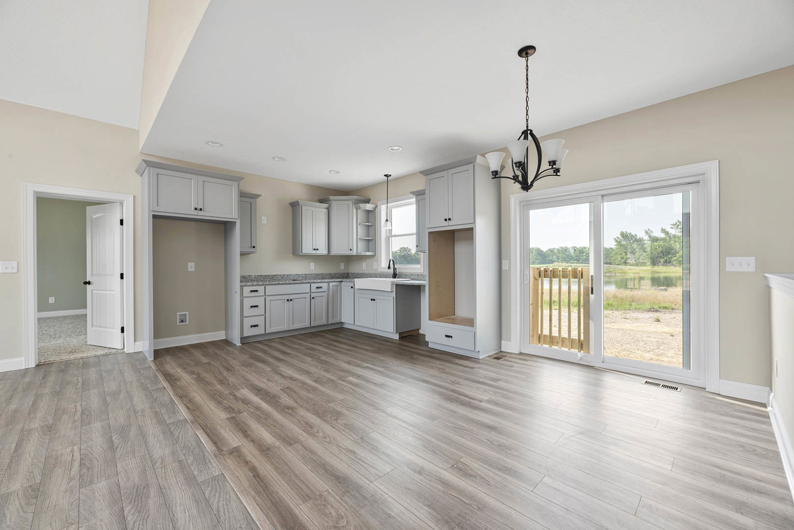 Wood flooring in a bright room featuring a large window and sliding glass door overlooking a lake and grassy yard, with a white interior door and modern chandelier visible