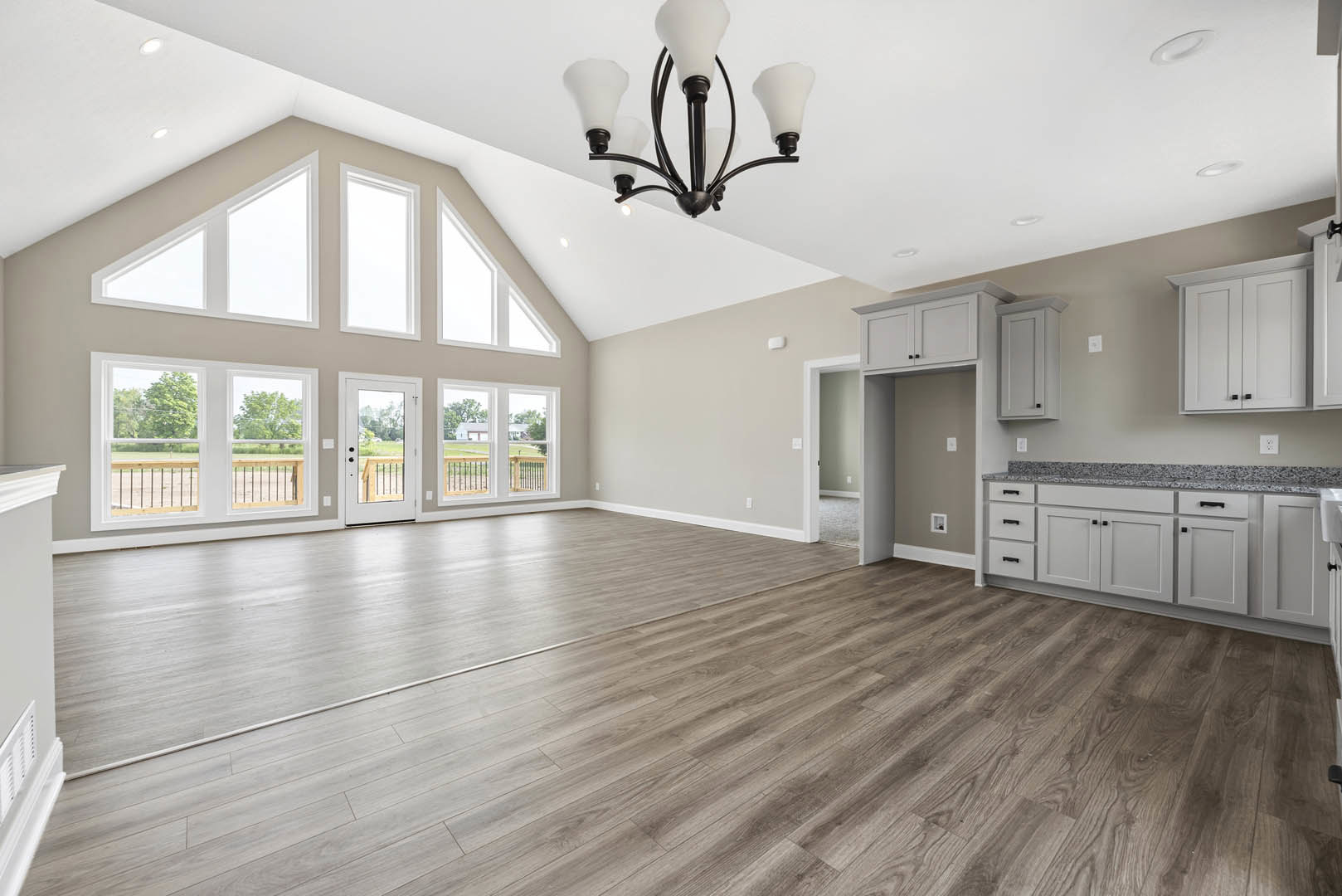 Spacious kitchen with hardwood floors, wood plank ceiling, modern chandelier, white cabinetry, stainless steel appliances, and large windows