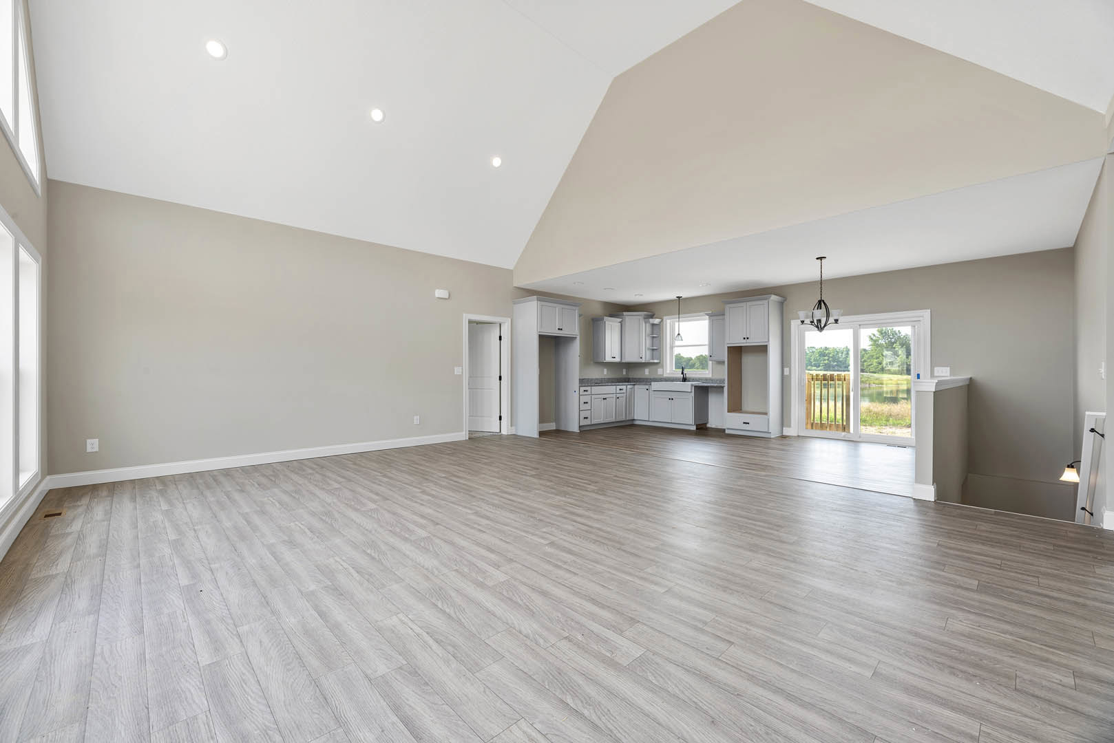 Spacious interior with hardwood flooring, wood plank ceiling, white walls, large window overlooking a lake, and white door with black handle