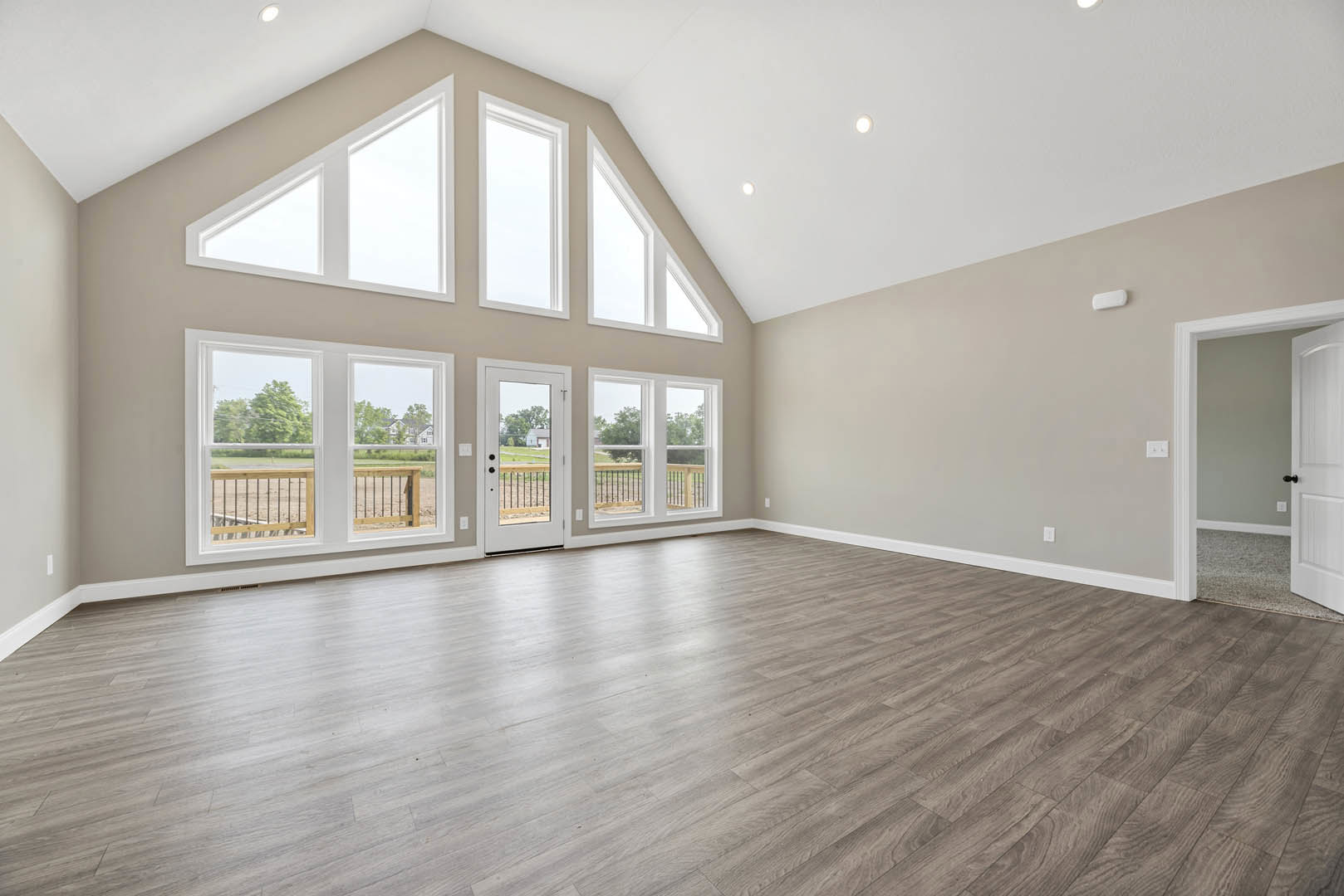 Spacious room with hardwood flooring, multiple large windows, white walls, and an open glass door leading to adjacent space