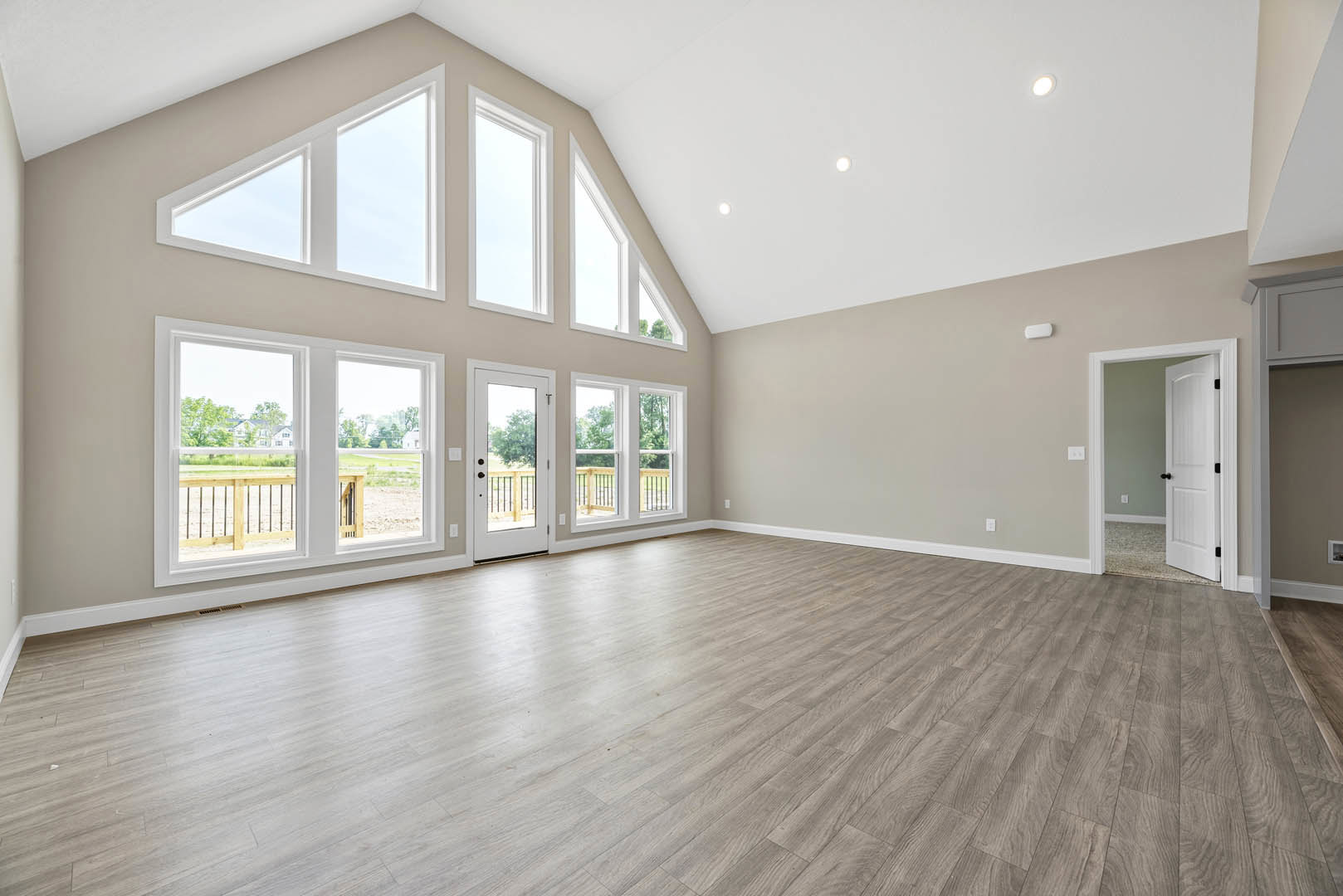 Spacious room with hardwood flooring, white door featuring glass panes and black knobs, large window overlooking a green yard