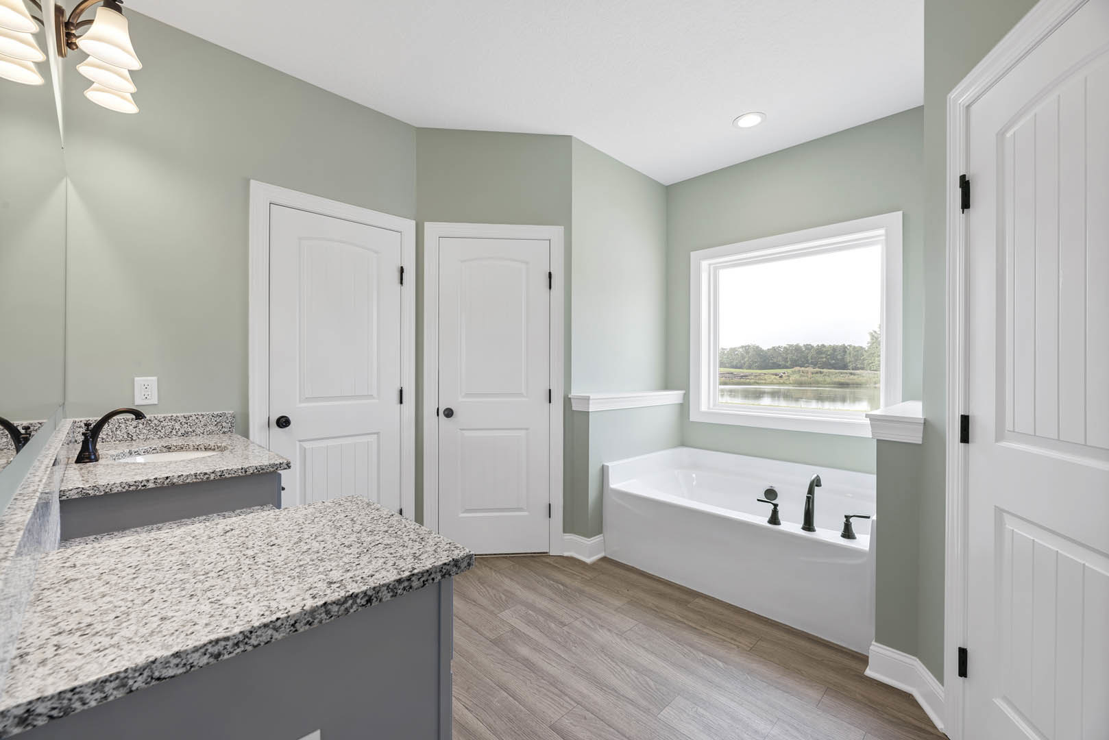 Bathroom featuring marble countertops, freestanding tub with chrome faucets, wood flooring, white door with black knob, window overlooking lake, and modern light fixture