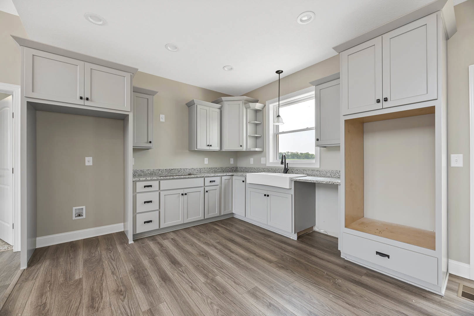White kitchen cabinets with brushed metal handles, wood plank flooring, light gray walls, quartz countertops, stainless steel sink, and recessed lighting.