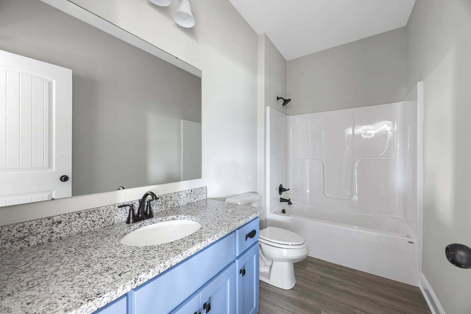 Marble countertop with white sink and black faucet, blue cabinetry below, freestanding bathtub, white toilet, tile flooring, white door partially visible