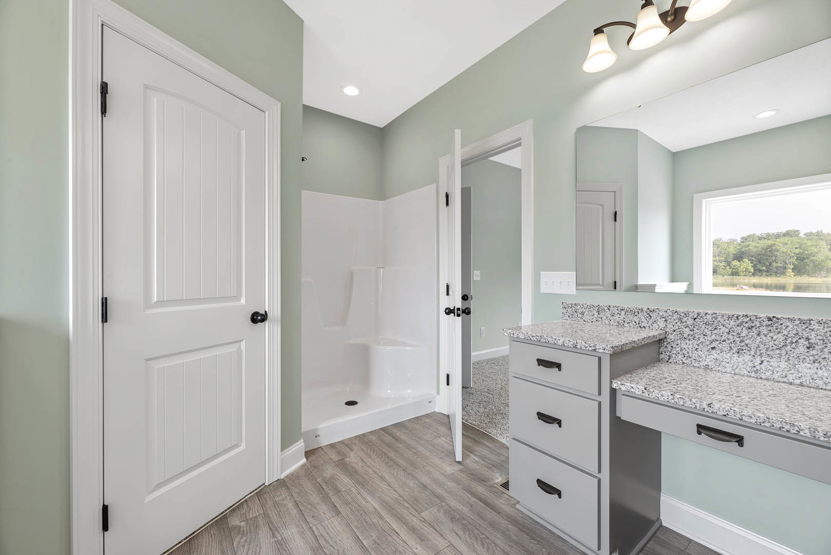 Modern bathroom featuring a white vanity with black hardware, curved corner shower stall, light fixture, and window overlooking forest scenery
