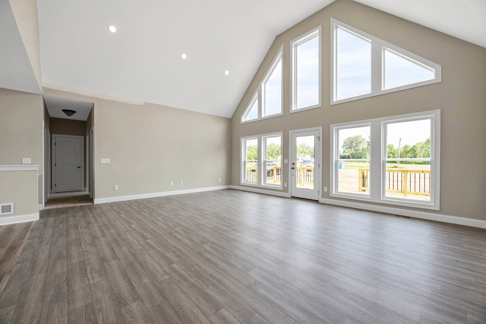 Spacious room featuring hardwood flooring, white walls, large windows overlooking a field, and a white door with black knobs.