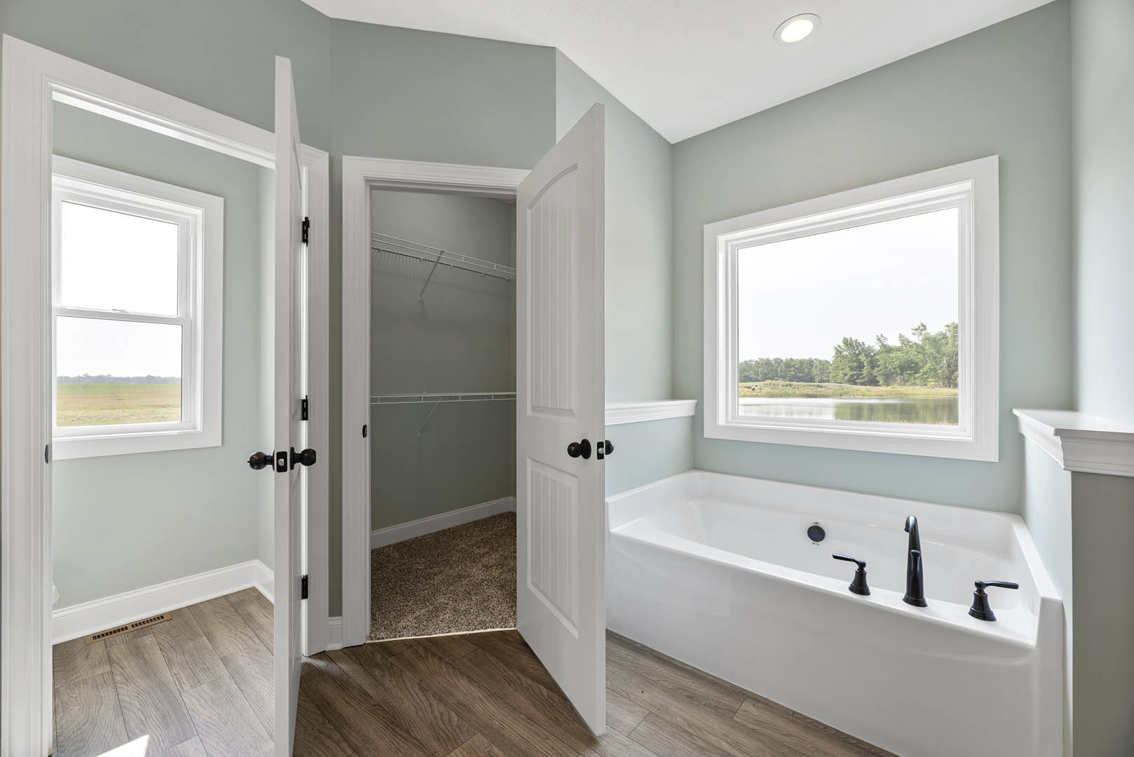 Bathroom with freestanding bathtub and glass-enclosed shower, wood flooring, ceiling light, large window overlooking lake and trees