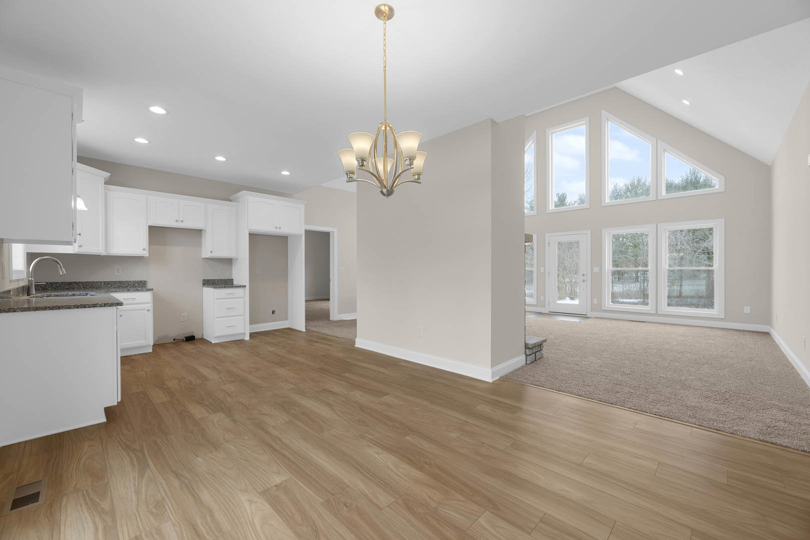 Spacious room with hardwood flooring, ornate chandelier, white cabinetry with silver handles, marble countertop, and neutral walls