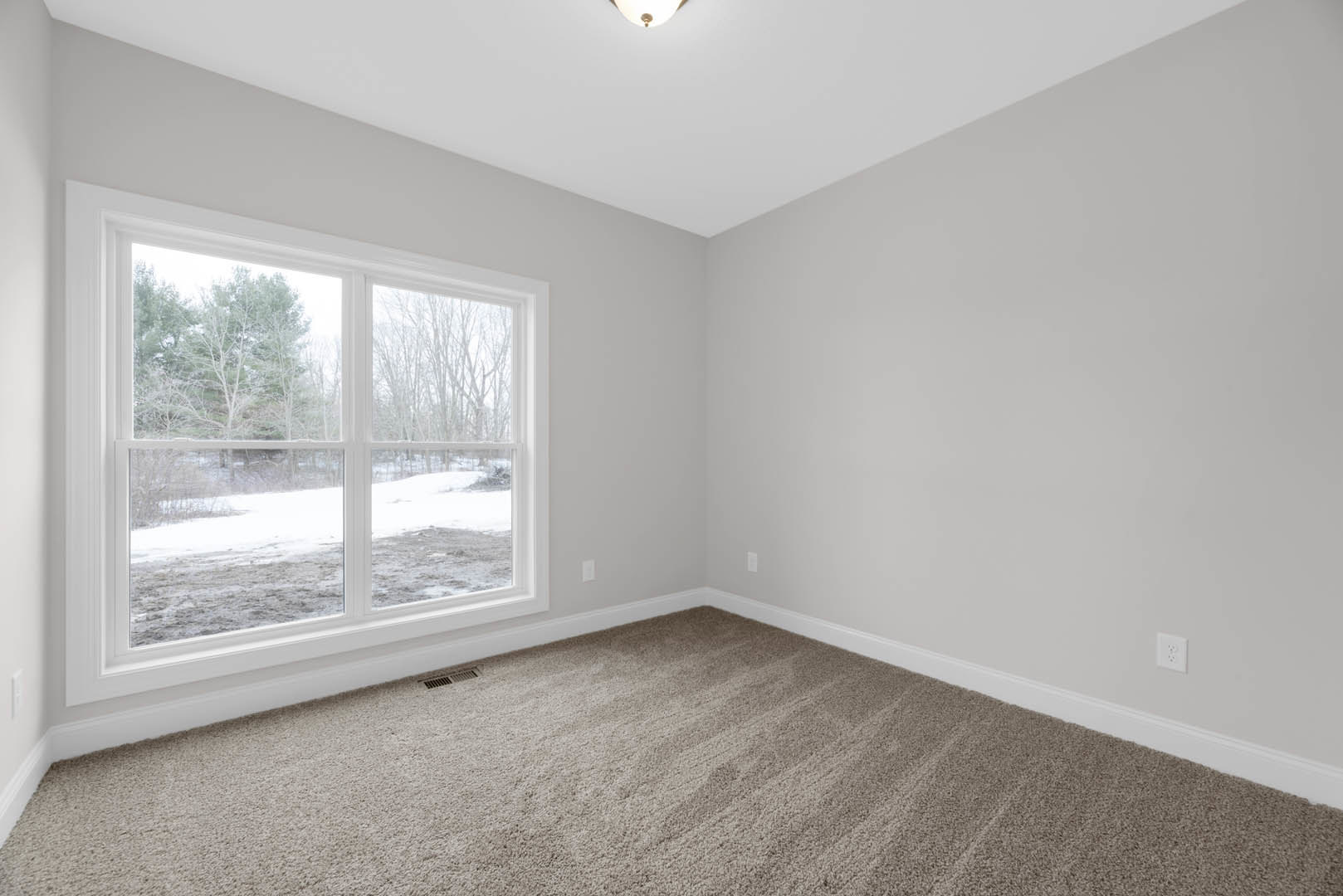 Neutral-toned carpeted room with white ceiling and recessed light, large window overlooking snow-covered ground and leafless trees