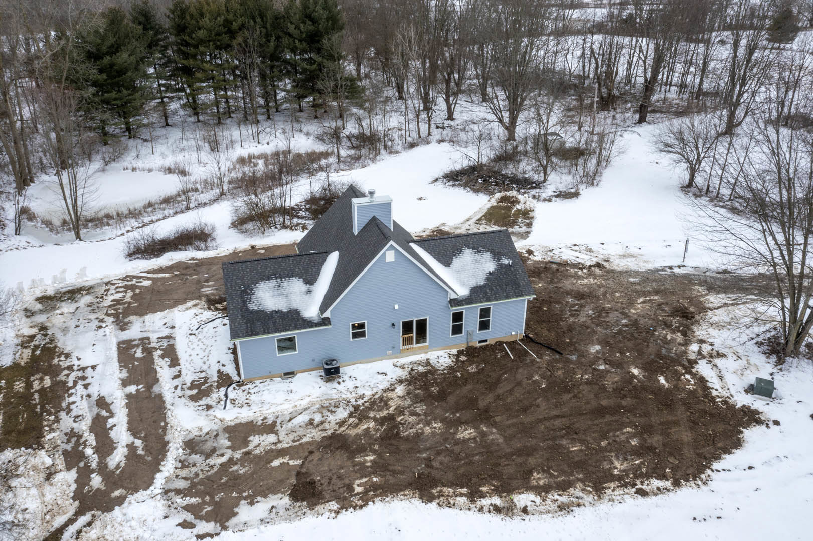 Modern house under construction surrounded by snow, wooden window railing, green square object in front, trees in snowy winter landscape