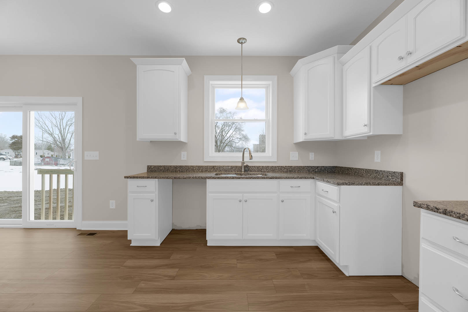 White kitchen cabinets, stainless steel sink beneath a window, wood flooring, pendant light with fabric shade, quartz countertops