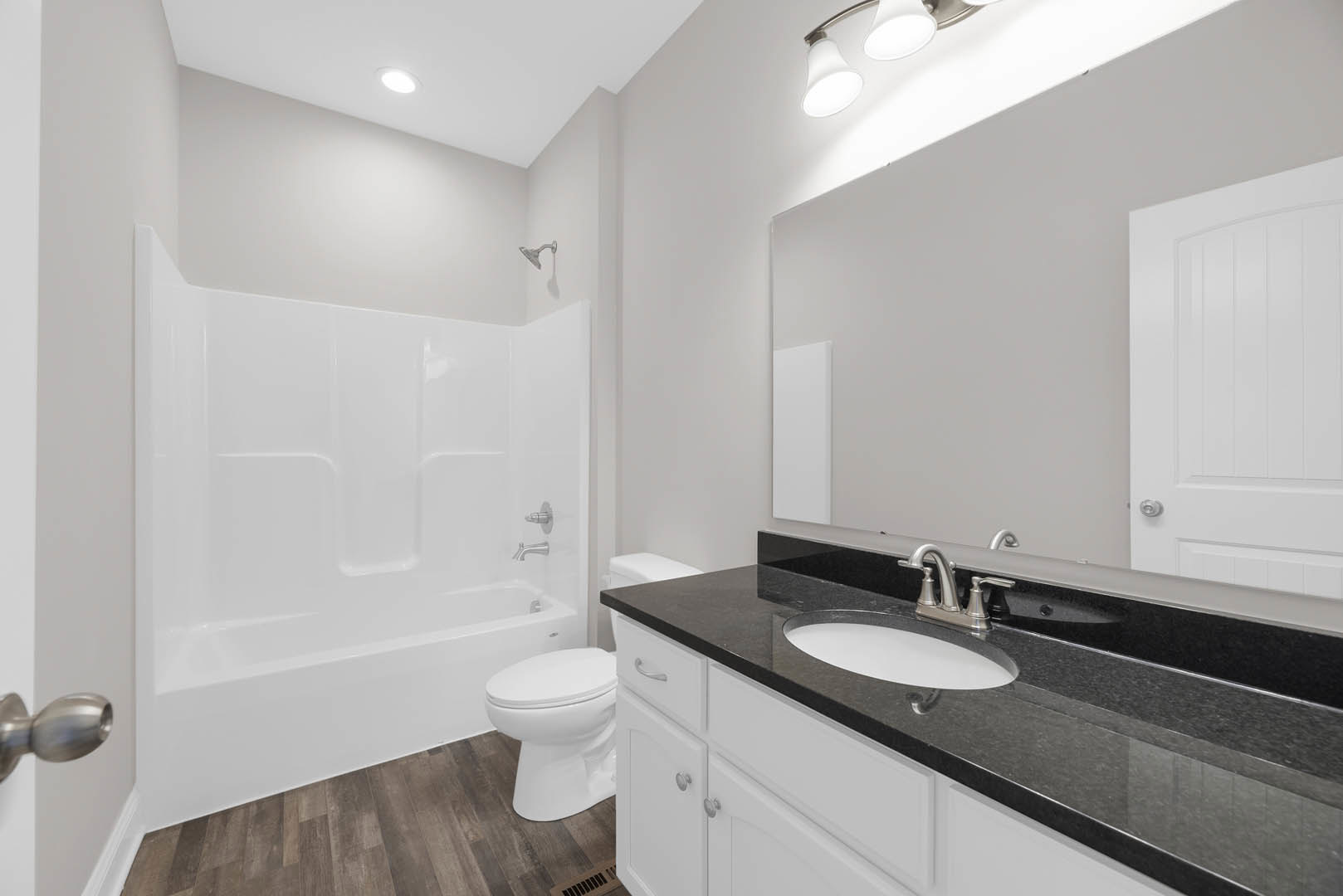 Bathroom with black stone countertop, white freestanding bathtub, paneled white wall, wall-mounted shower head, close-up of modern sink, and covered toilet.