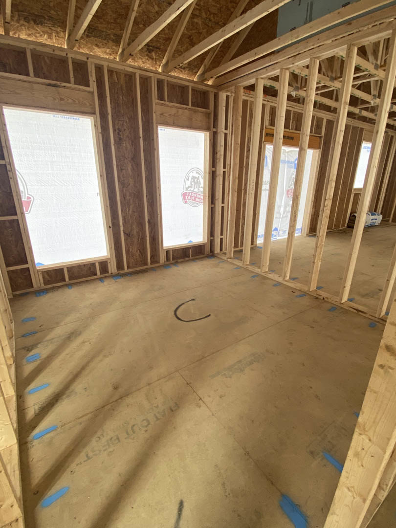 Room with exposed wood ceiling beams, several rectangular windows, white walls, and construction materials visible.