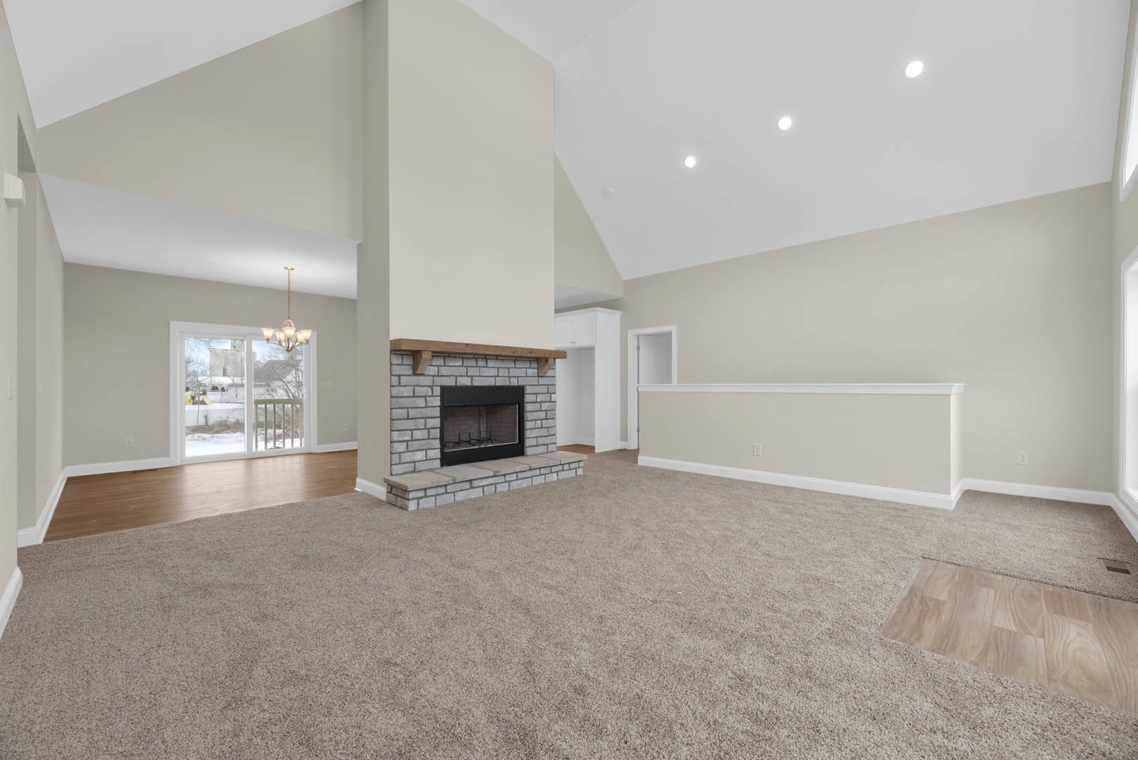 Living room featuring a carpeted floor, central fireplace with glass window, plaster walls, sliding glass door overlooking snowy yard, and laminate wood flooring with area rug.