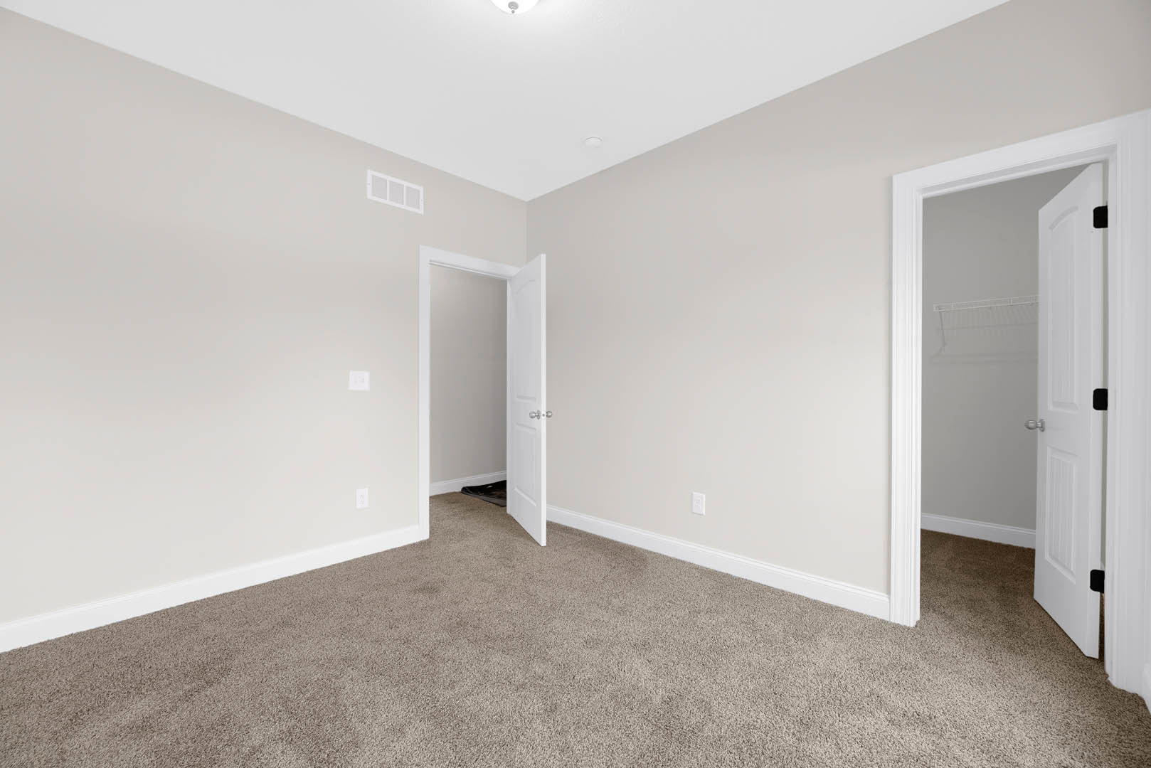 White paneled door with silver knobs open onto carpeted floor, white shelving unit and square-paned window visible against light plaster walls