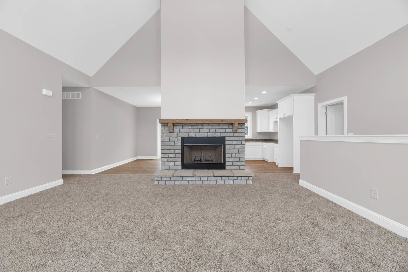 Living room with light carpet flooring, central black-framed fireplace set in a brick wall, white door with metal frame, plaster walls, and neutral interior finishes.