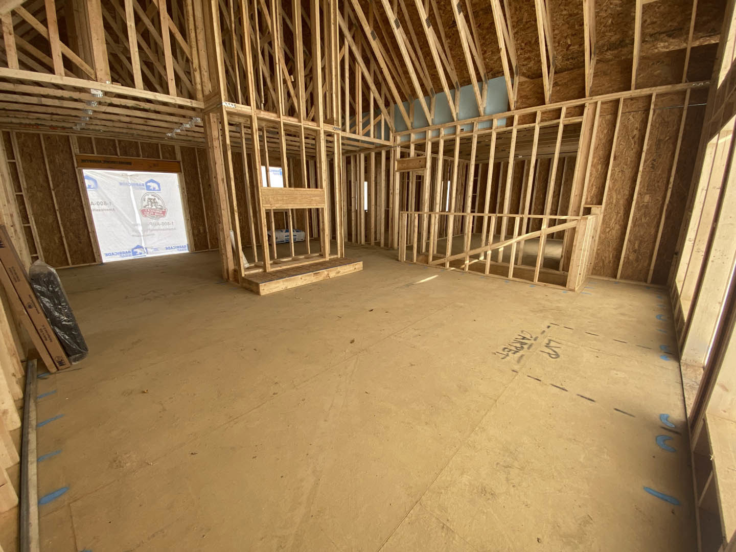 Wood-framed room with exposed beams, unfinished wooden floor, white plastic bag with blue and red logos, and a cardboard box on the ground