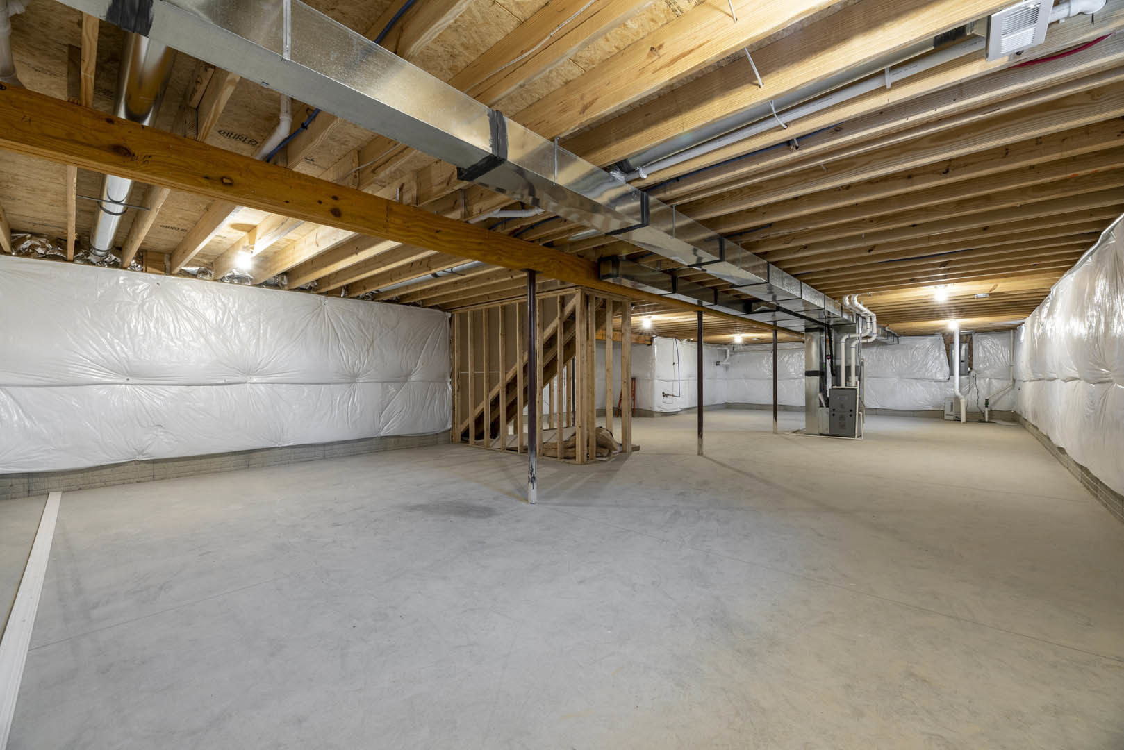 Exposed wood beams and metal pipes on ceiling, white plastic covering, concrete floor with wooden framing, close-up of white wall