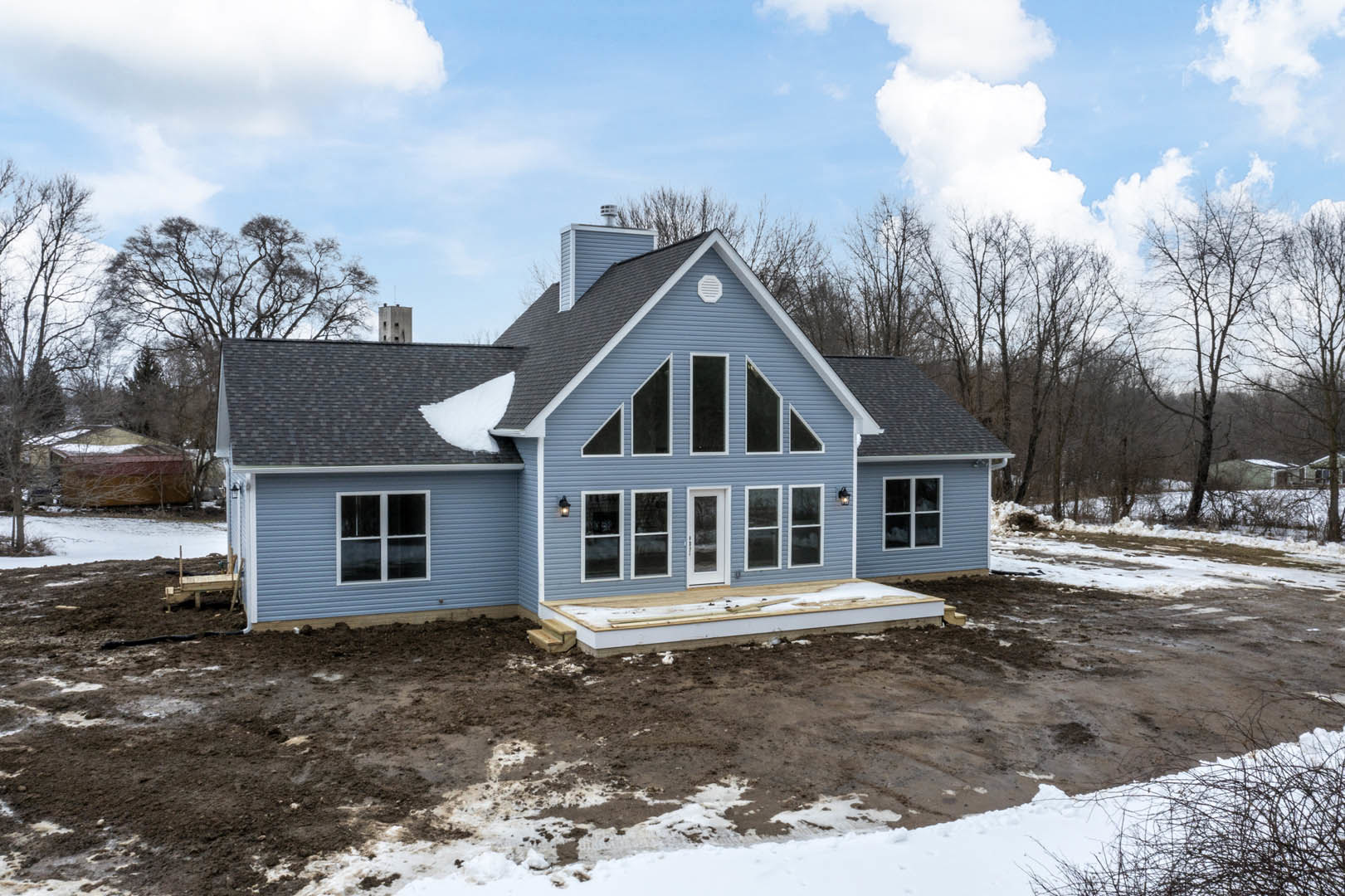Modern home with snow-covered roof and ground, white-framed windows, winter trees, and overcast sky