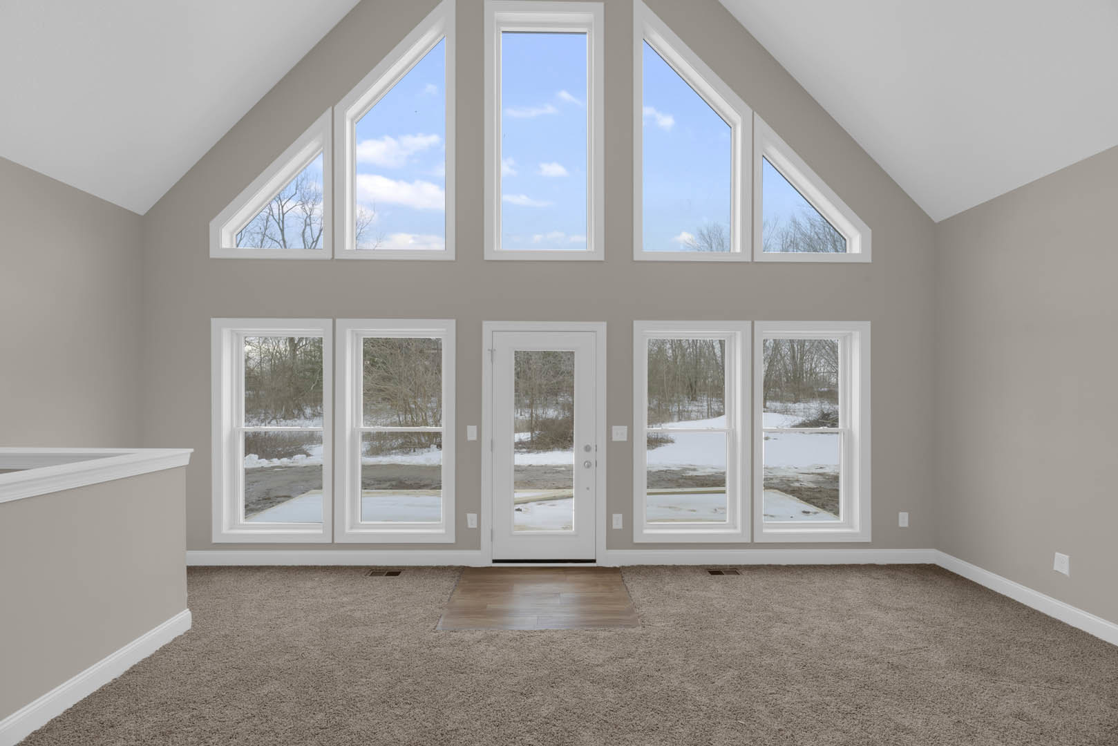Spacious room featuring multiple large windows with blue sky views, square tile and carpet flooring, wood floor detail, white molding, and a door.