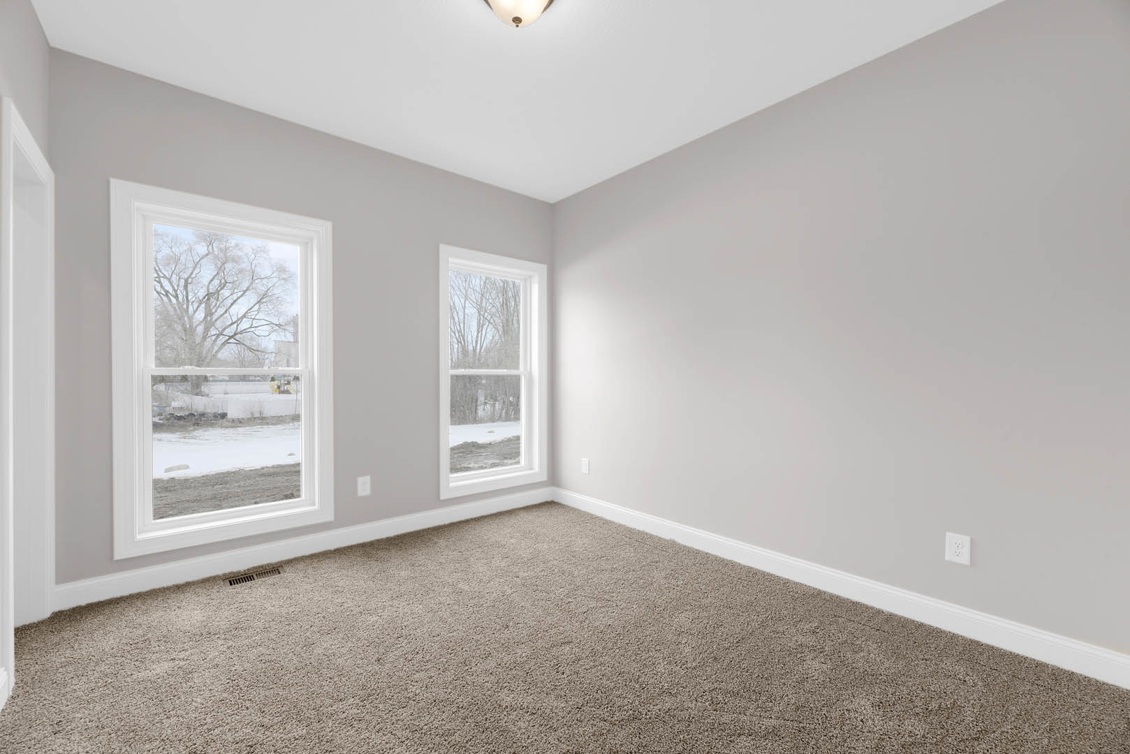 Spacious carpeted room featuring large windows with views of snowy trees, white ceiling with recessed lighting, and neutral walls with crown molding.