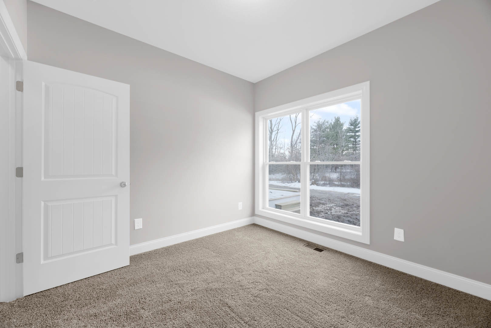 Carpeted room with white walls, white ceiling, white door with silver handle, large window overlooking snowy field, laminate flooring near door, simple molding along baseboards