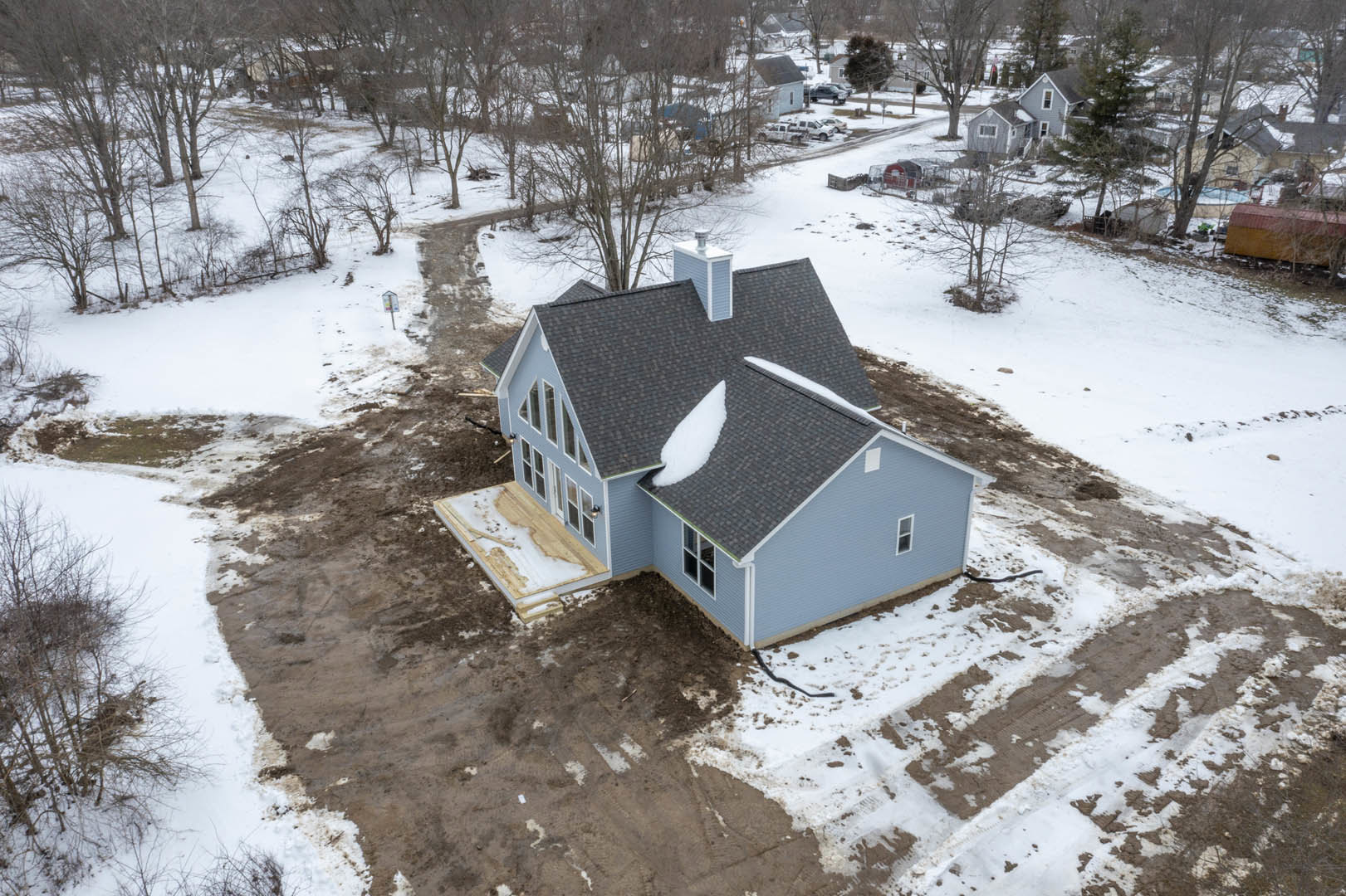 Partially built house with exposed framing and snow covering the roof and ground, leafless tree nearby, winter landscape