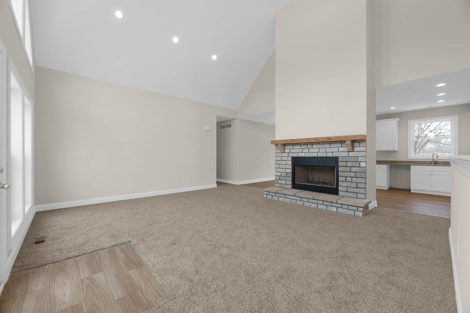 Living room with beige carpet, white fireplace with glass door, white cabinets with wooden tops, recessed ceiling lights, and neutral plaster walls.