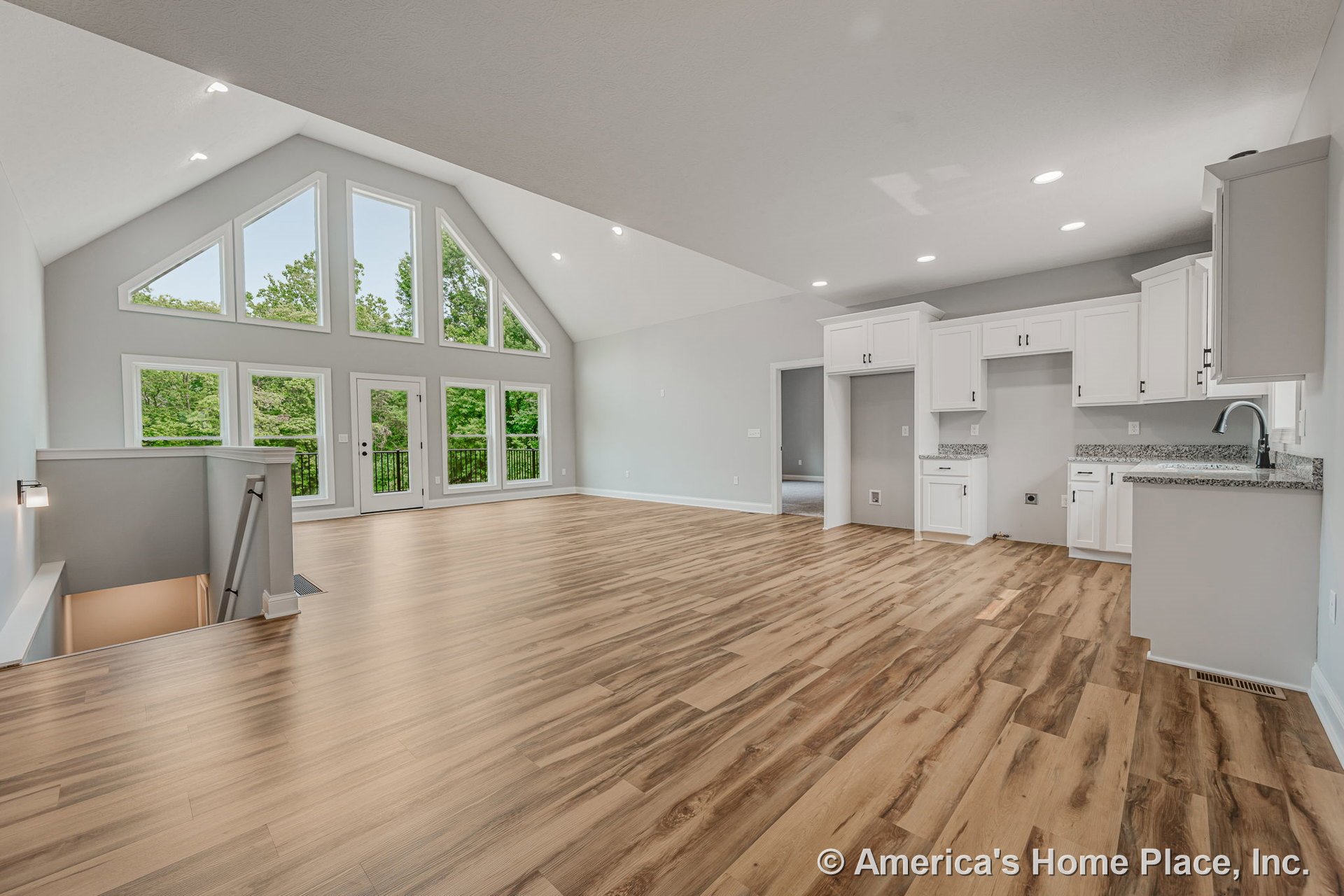 Vaulted ceiling living area with triangular window wall, open concept layout, modern kitchen featuring white cabinetry and granite countertops, wood-look flooring, recessed