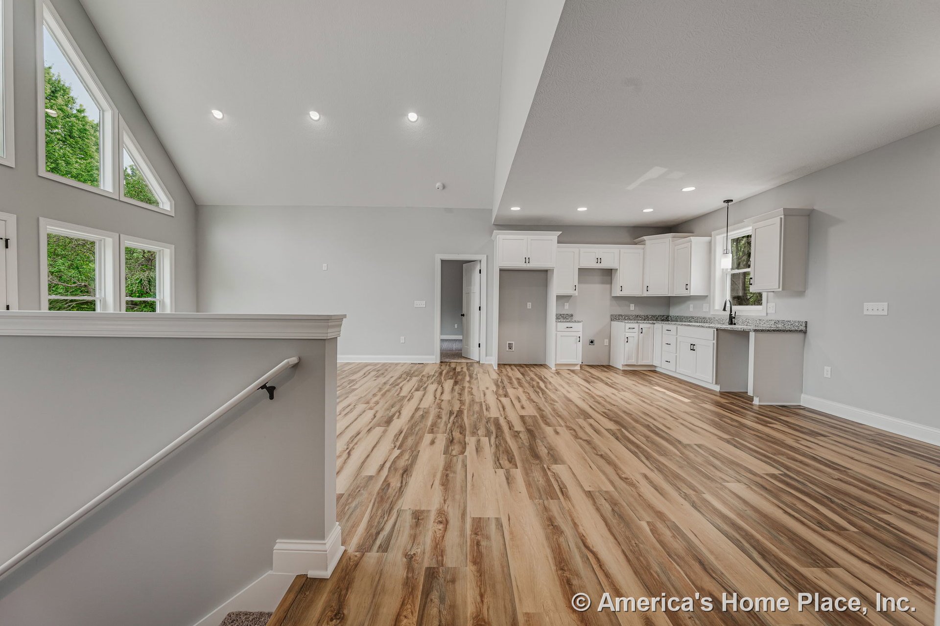 Vaulted ceiling with recessed lighting, expansive triangular and rectangular windows, open-concept kitchen featuring white cabinetry and granite countertops, wood-look plank