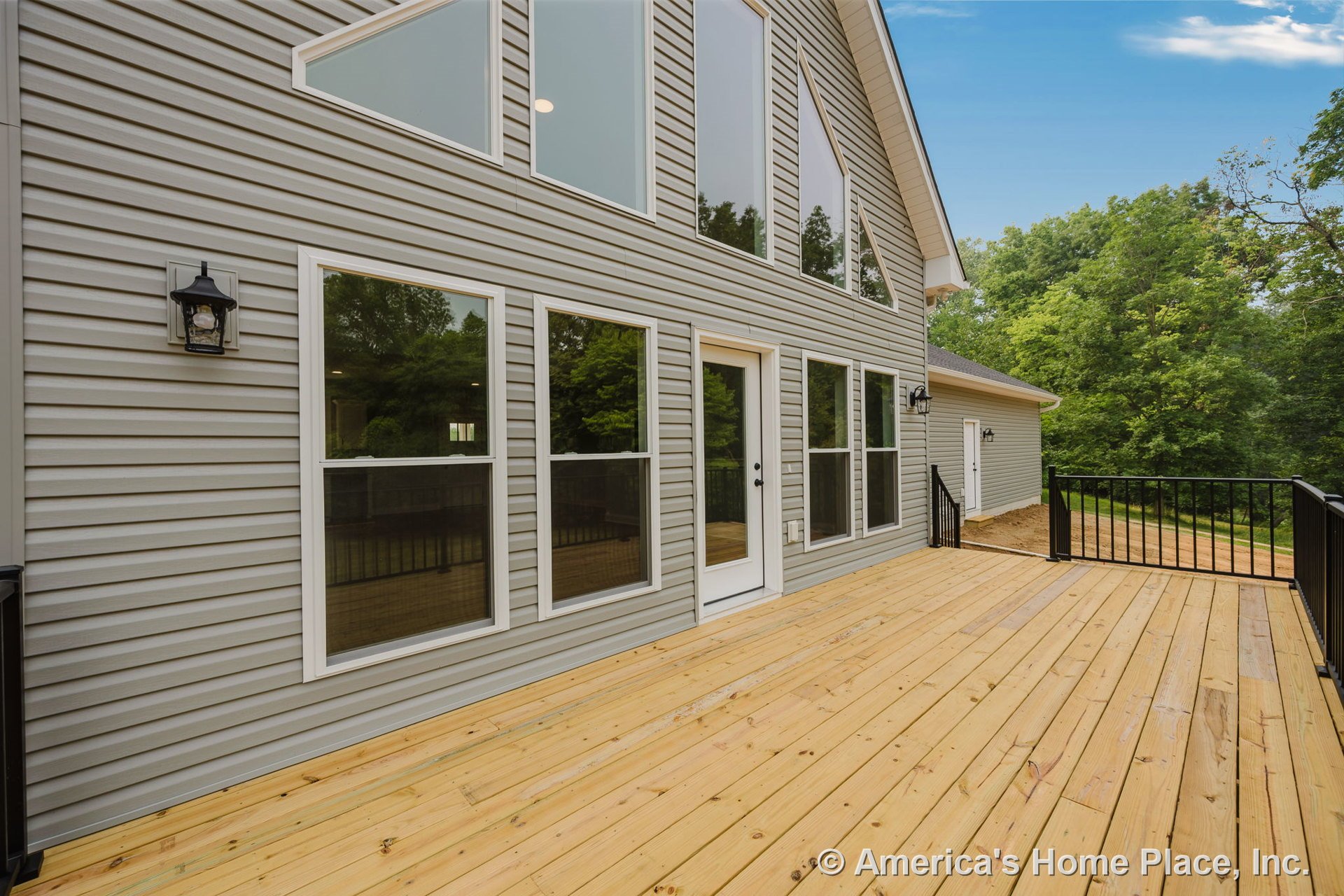Spacious wood plank deck with black metal railing, attached to a modern home featuring gray vinyl siding, large rectangular windows with white trim, exterior wall-mounted lights