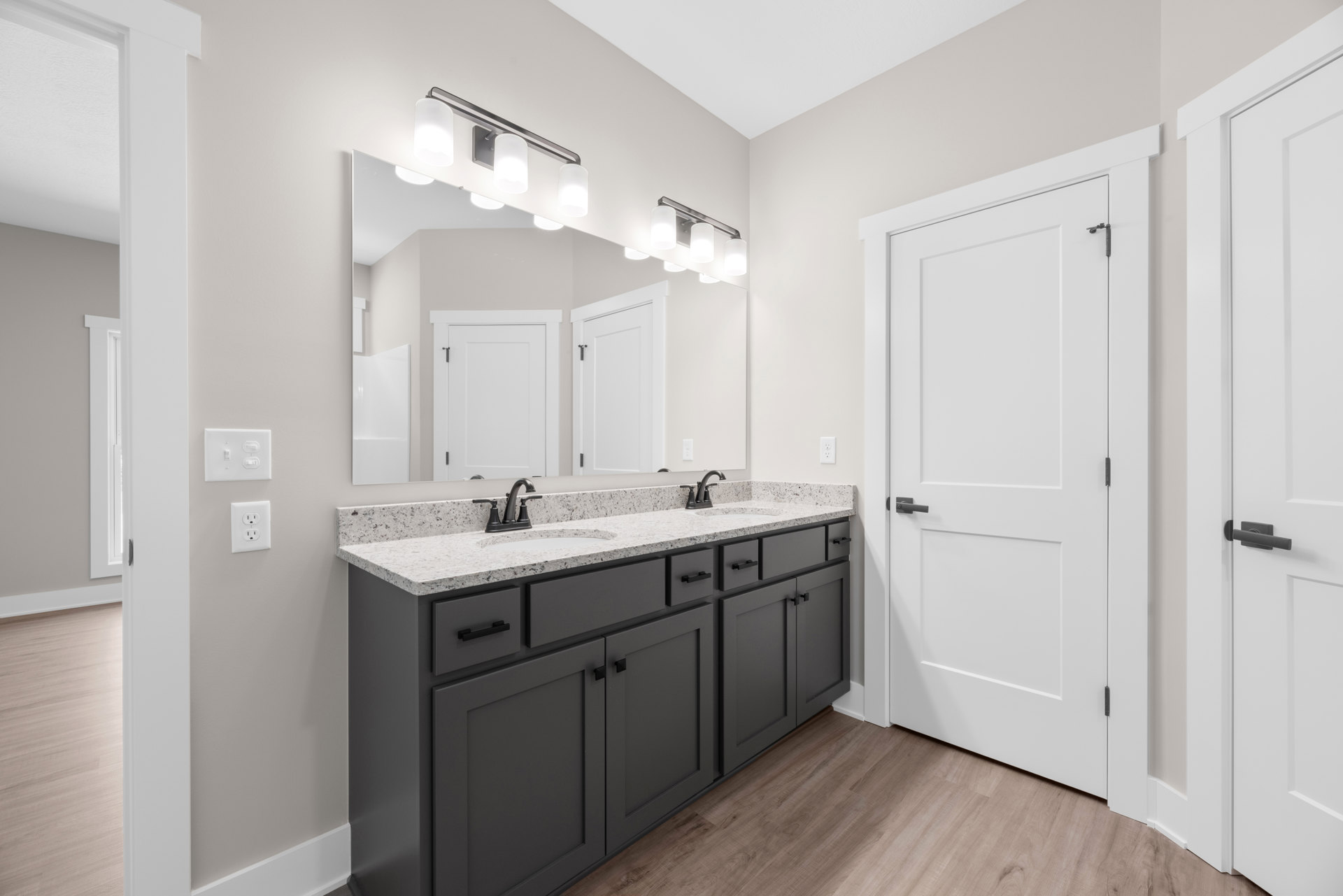Bathroom with double sinks, white cabinetry, stone countertop, large wall mirror, chrome faucets, and light tile flooring