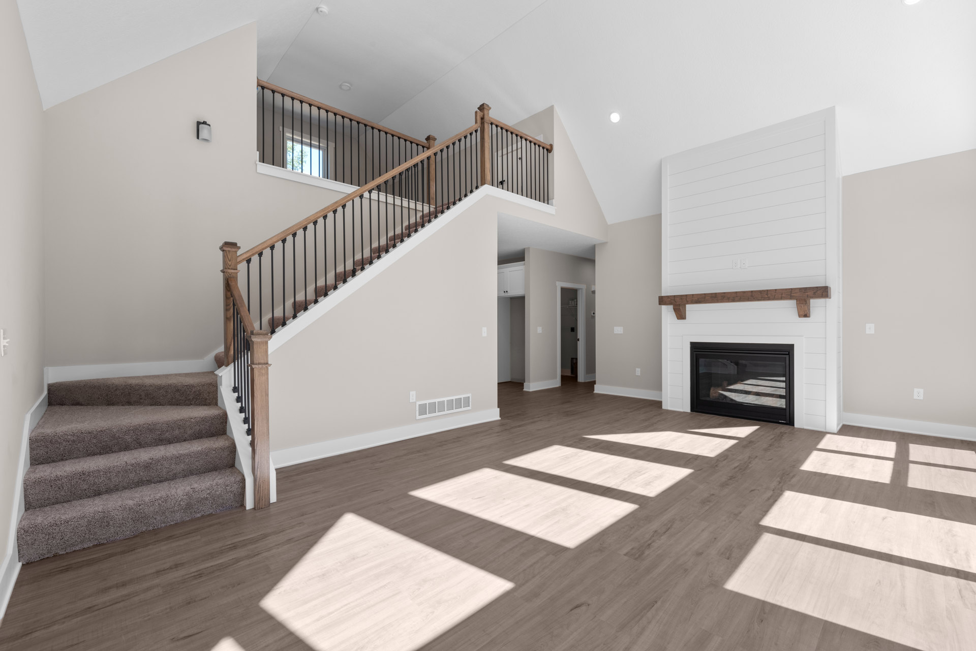 Open living area with hardwood floors, carpeted staircase featuring iron railings, plaster walls, and a fireplace with a glass door