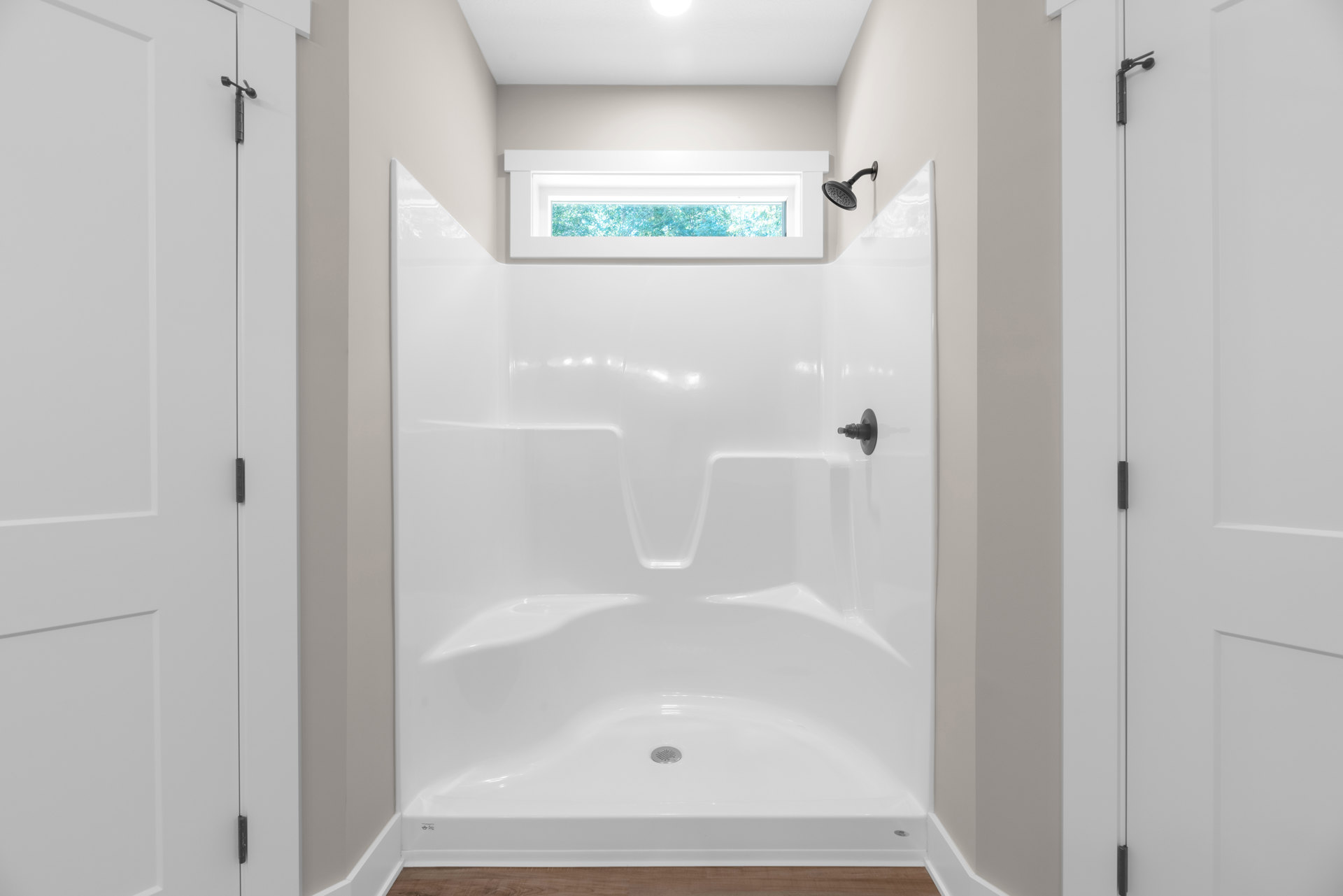 White tile shower with black showerhead, window with white frame, and built-in bathtub with chrome drain