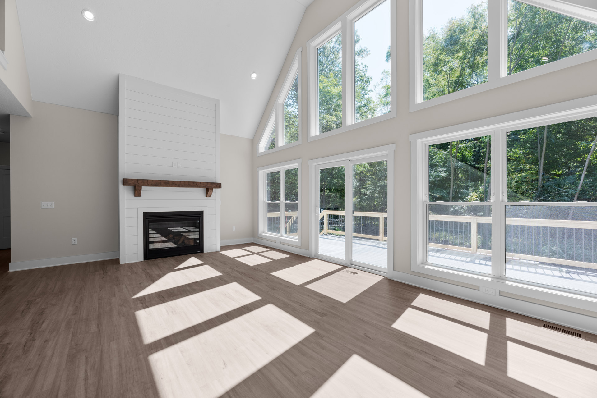Living room with white walls, large windows, black fireplace with stacked wood, wooden ceiling beam, and light wood flooring.