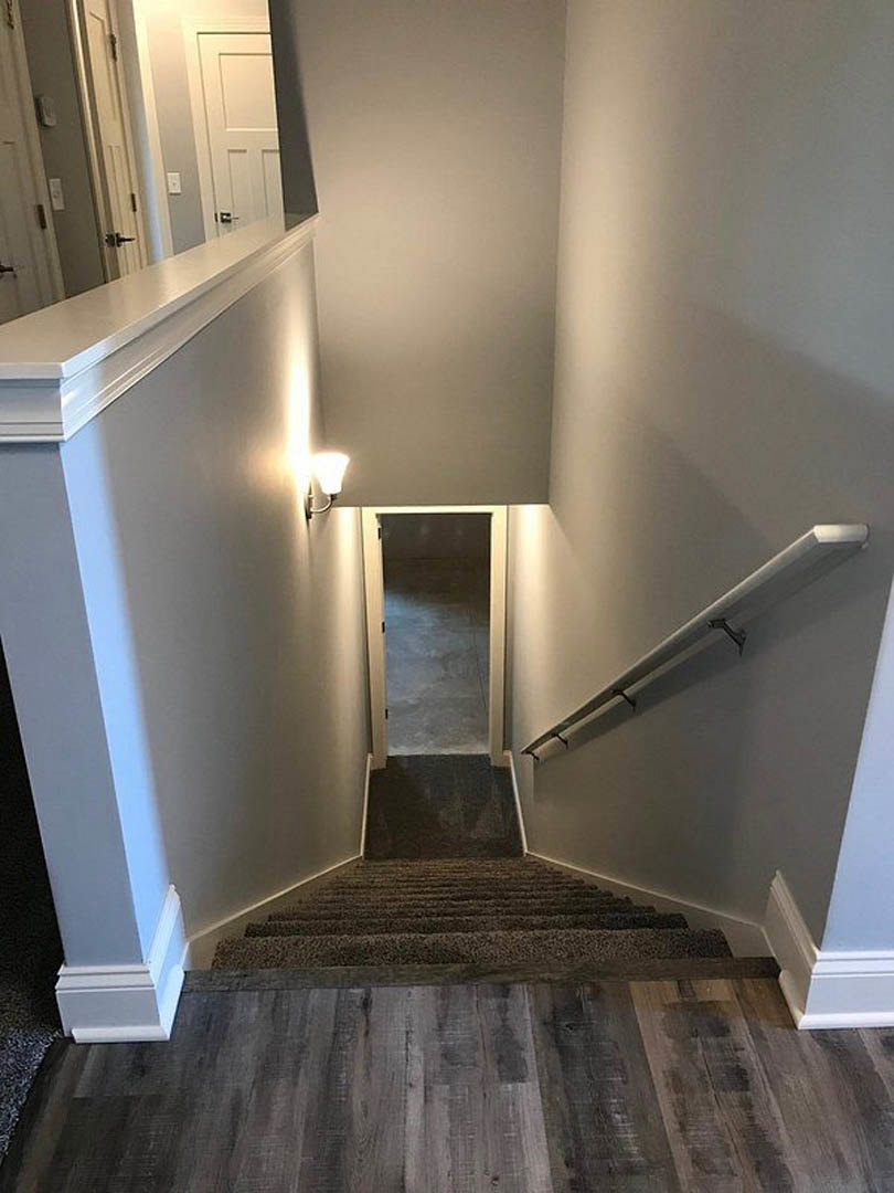 Wood staircase with metal railing, light fixture mounted on plaster wall, hardwood flooring, open doorway leading to adjacent room.