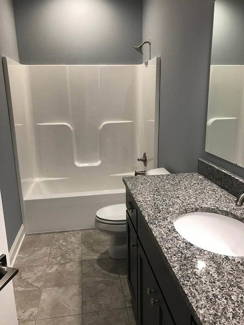 Marble countertop with undermount sink, chrome faucet, white tile floor, partial view of toilet and bathtub, wall-mounted mirror above vanity