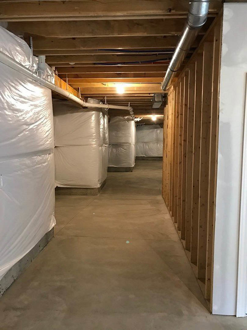 Hallway under construction with white plastic bags and rolls, exposed wooden framing, plaster walls, and metal pipe along unfinished floor.