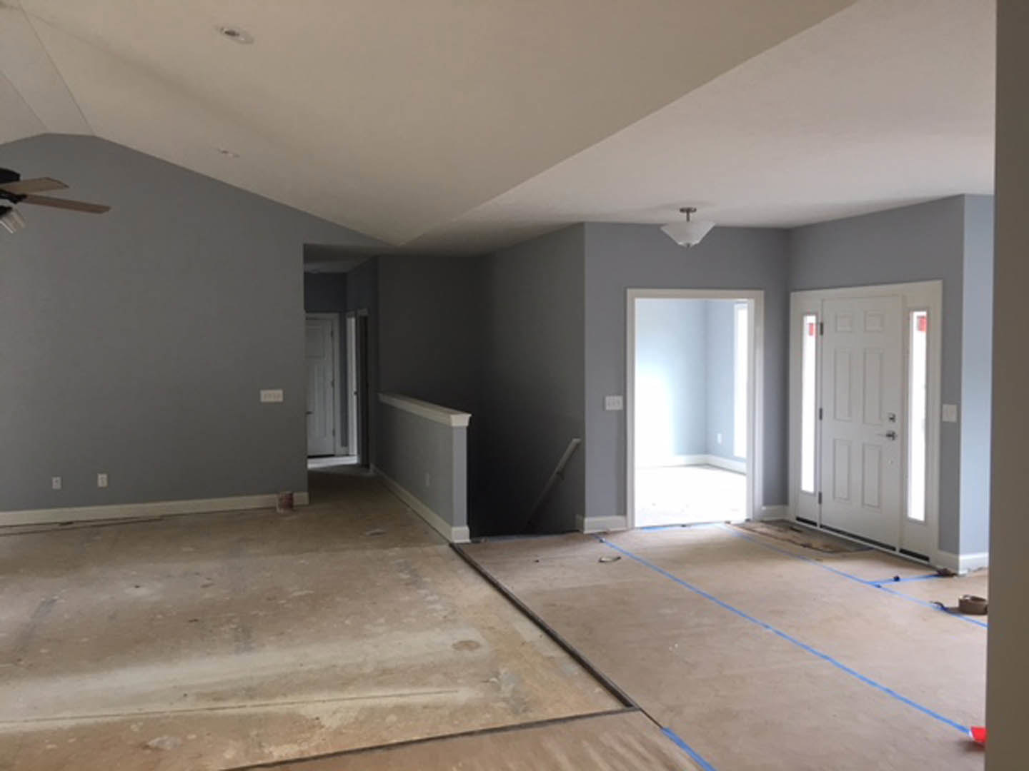 White paneled door with black handle set in a white wall, blue painter’s tape on light-colored flooring, soft natural light filtering through doorway.