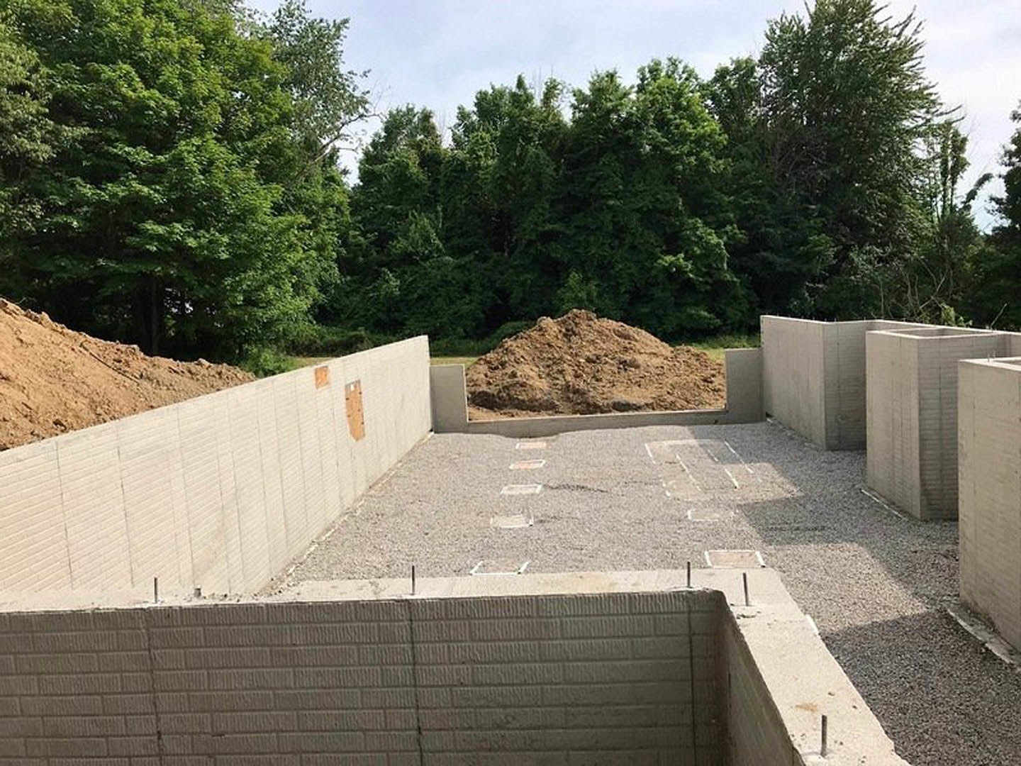 Concrete foundation surrounded by piles of dirt, trees, and open sky in the background