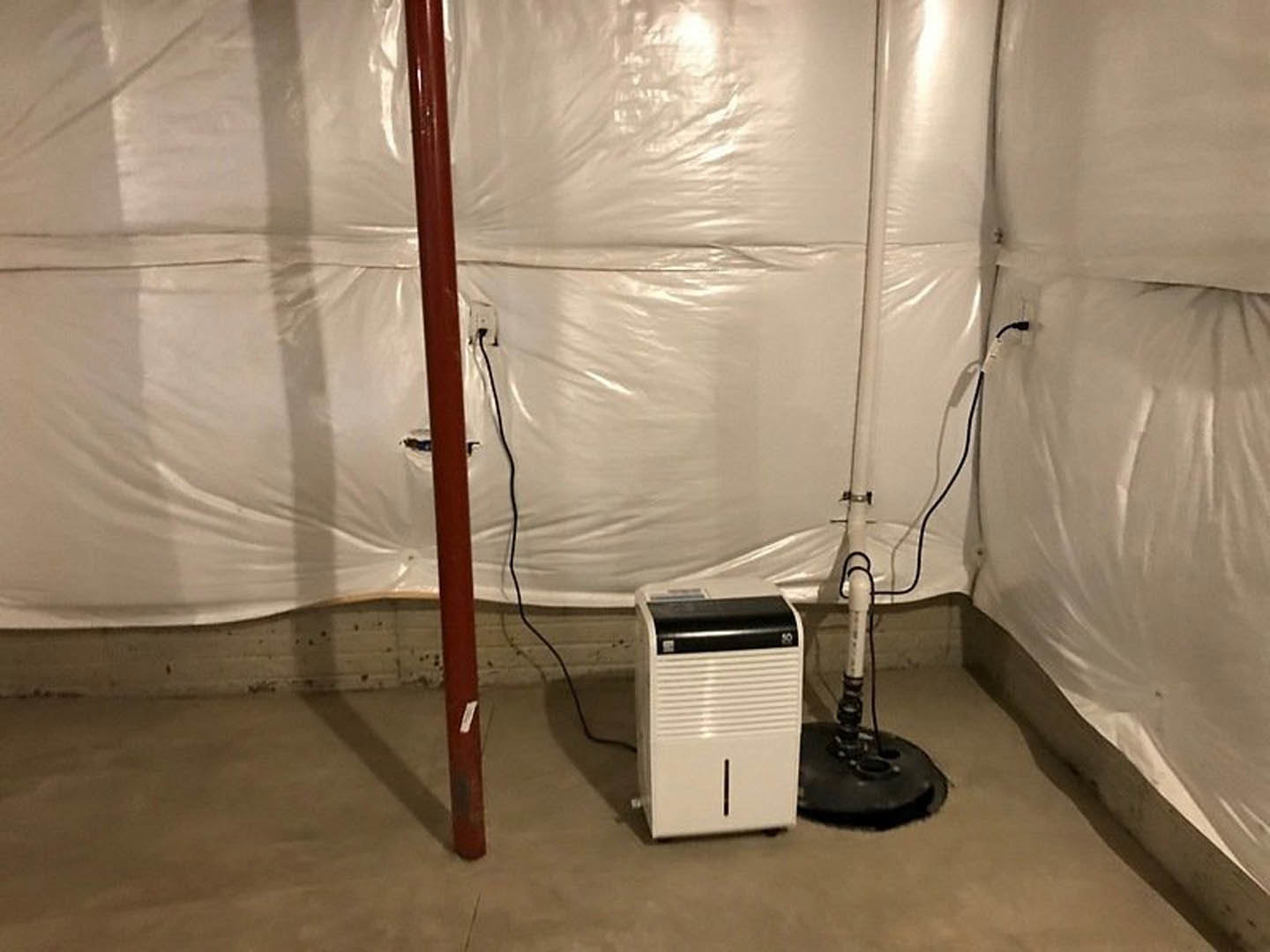 White rectangular appliance with black cord positioned beside a red metal pole on indoor tile flooring, adjacent to a painted wall.